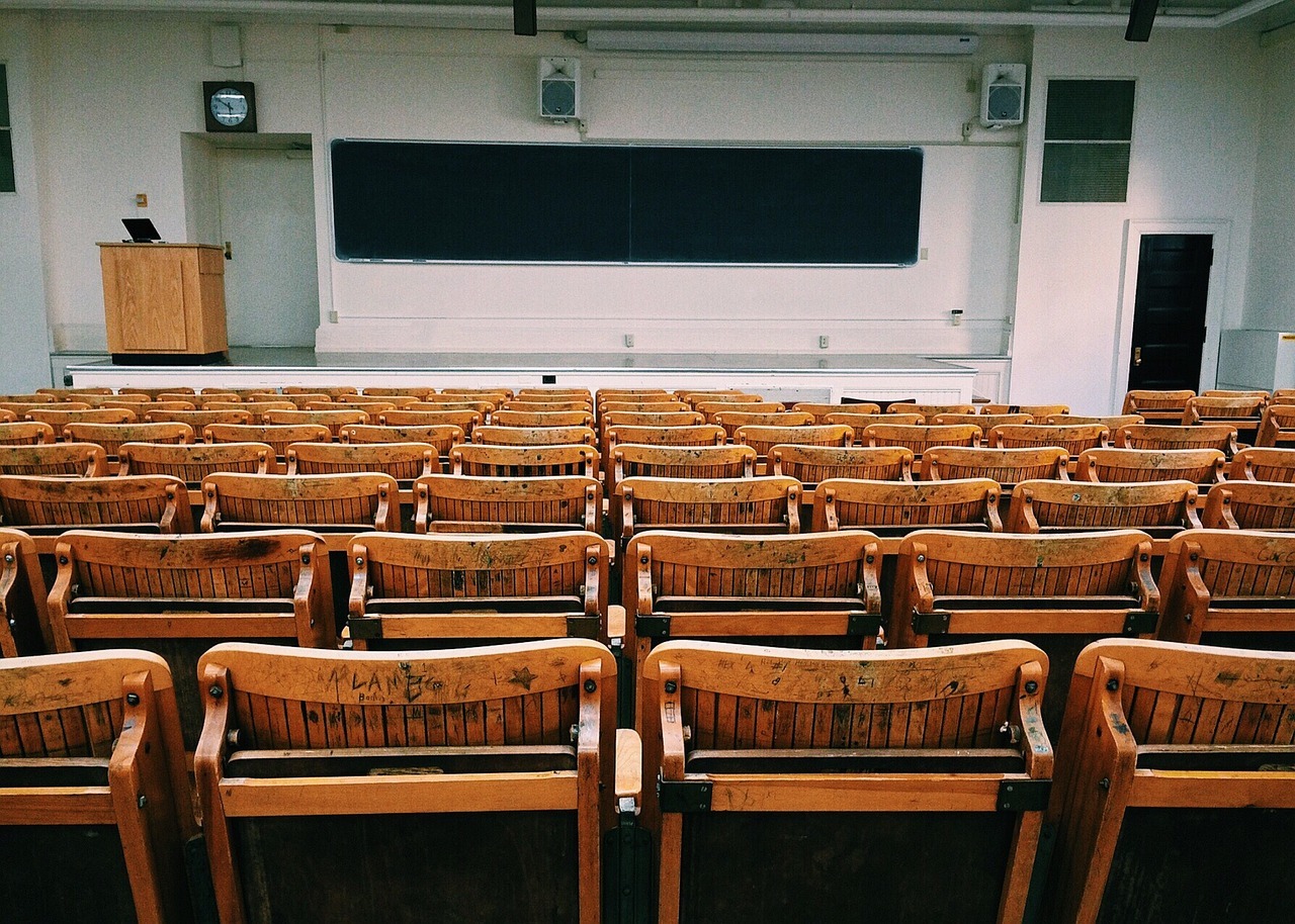 classroom lecture style room with chairs facing screen and podium